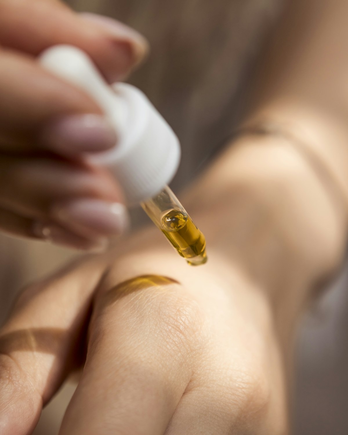 A dropper releasing facial oil onto the back of a hand